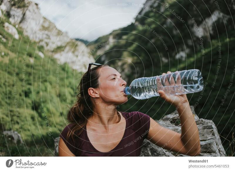 Mid adult female trekker drinking from plastic water bottle while looking away color image colour image Las Xanas Route Spain outdoors location shots