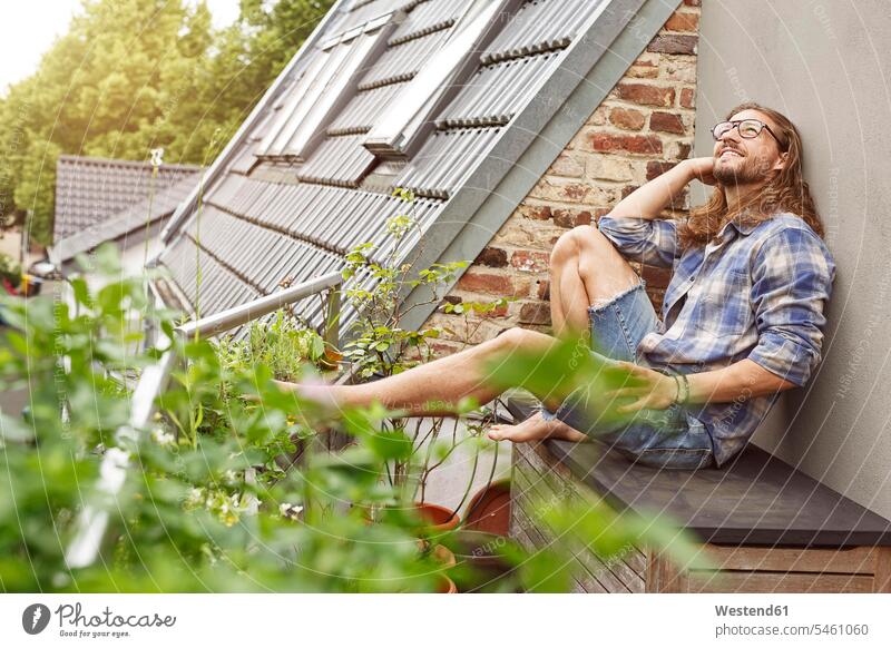 Happy young man sitting on his balcony, relaxing Plant Plants young men happiness happy Seated relaxation balconies males Adults grown-ups grownups adult people
