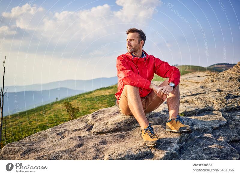 Man sitting on rock enjoying serene moments during hiking trip hike indulgence enjoyment savoring indulging mountain mountains man males Seated rocks pleasure