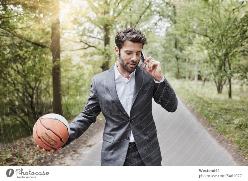 Businessman with basketball talking on smartphone on rural road on the phone call telephoning On The Telephone calling Business man Businessmen Business men