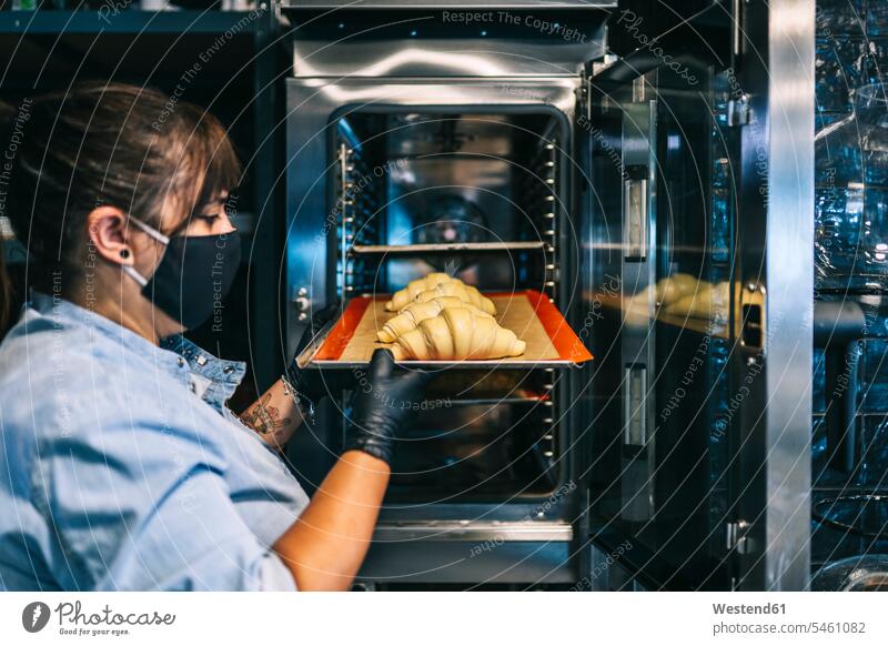 Female chef putting baking sheet with croissants in oven at restaurant kitchen color image colour image indoors indoor shot indoor shots interior interior view