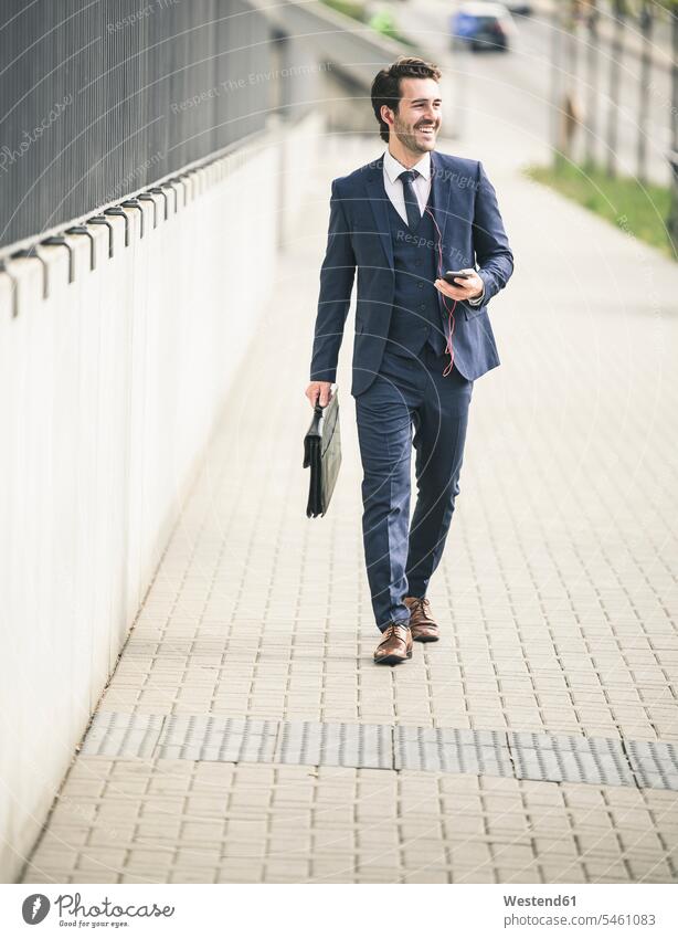 Happy businessman walking in the city with cell phone and earphones freelancer freelancing business world business life urban urbanity independence independent