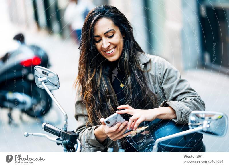Smiling biker woman using mobile phone on motorcycle in city color image colour image outdoors location shots outdoor shot outdoor shots day daylight shot