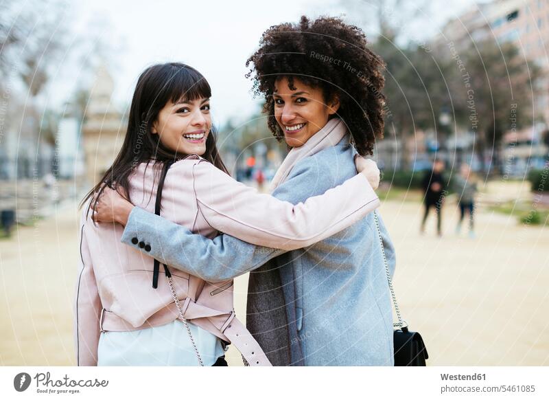 Spain, Barcelona, portrait of two happy women in city park embracing turning round female friends woman females town cities towns portraits parks happiness