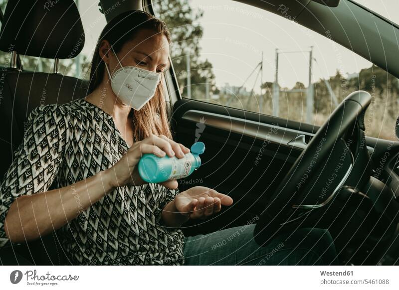 Mid adult woman with protective mask using sanitizer in car Bottles motor vehicles road vehicle road vehicles Auto automobile Automobiles cars motorcar