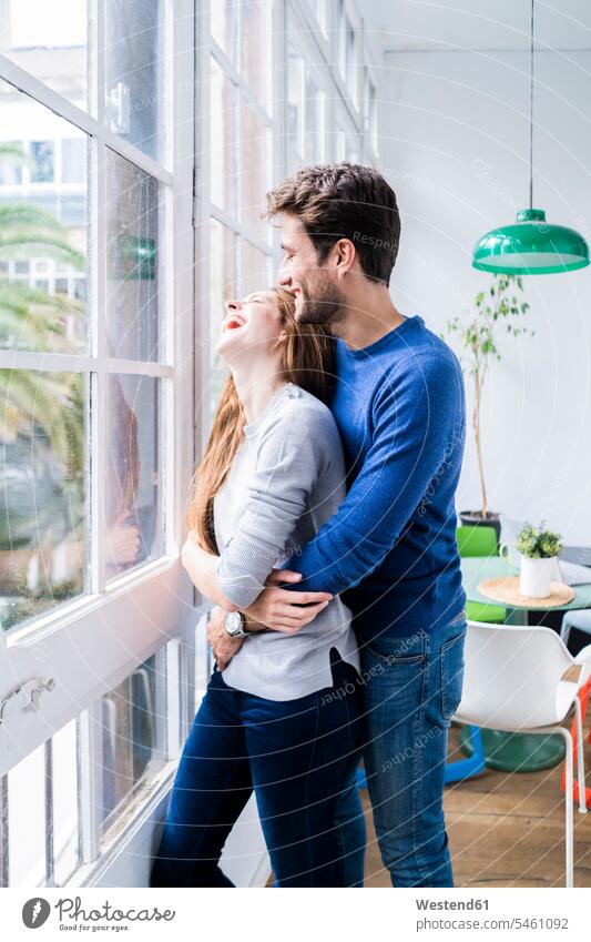 Happy affectionate couple hugging at the window at home windows jumper sweater Sweaters relax relaxing cuddle snuggle snuggling smile embrace Embracement