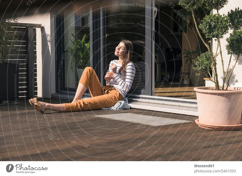 Young woman sitting on terrace at home enjoying the sunshine Germany sitting on ground Sitting On The Floor Sitting On Floor comfortable stripes striped