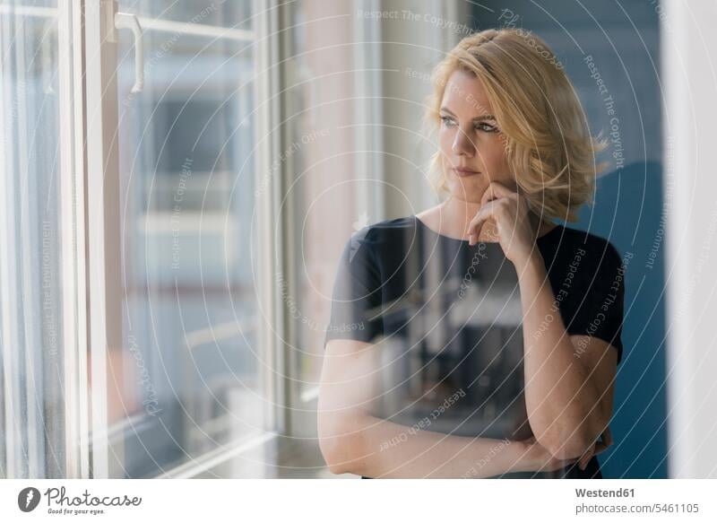 Serious blond woman looking out of window serious earnest Seriousness austere females women windows view seeing viewing blond hair blonde hair Adults grown-ups