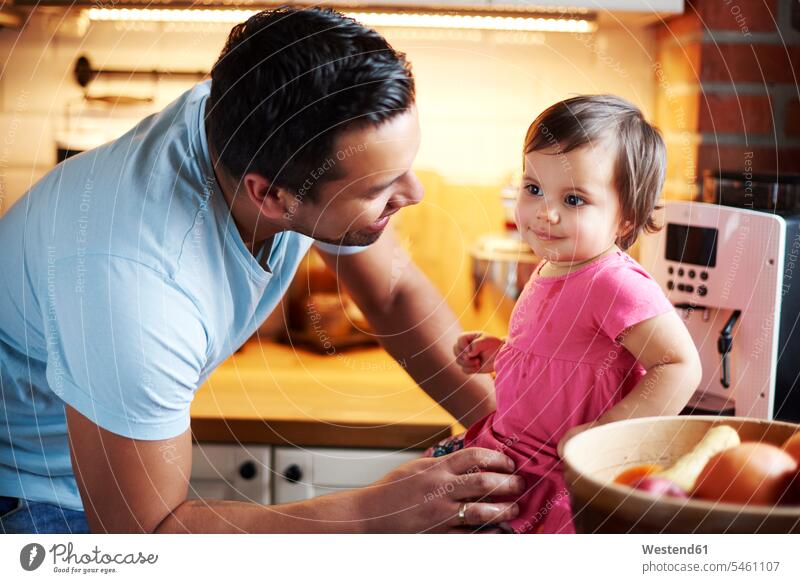 Smiling father looking at baby girl sitting on counter in kitchen at home kitchen counter countertops kitchen counters Kitchen Worktop infants nurselings babies