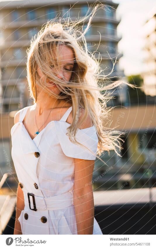 Blond young woman with windswept hair wearing white dress outdoors blond blond hair blonde hair females women dresses blowing people persons human being humans