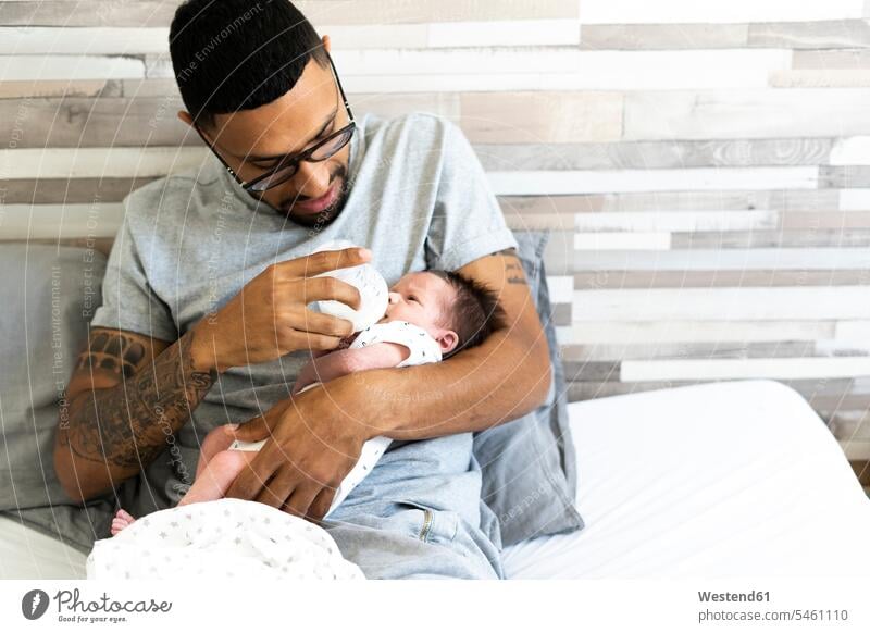 Father bottle-feeding his newborn baby in bed multicultural beds protecting infants nurselings babies baby bottle feeding bottle feeding bottles baby bottles
