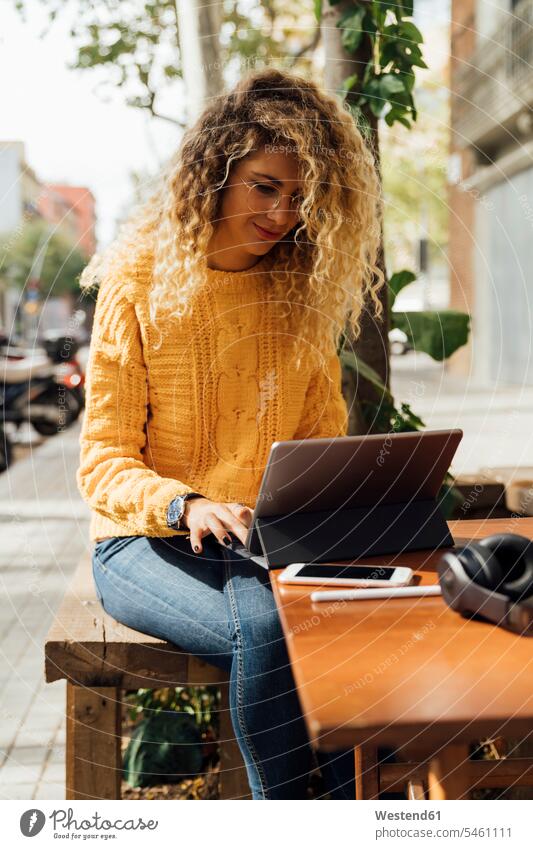 Beautiful blond female student using digital tablet while sitting at sidewalk cafe in city color image colour image Spain outdoors location shots outdoor shot