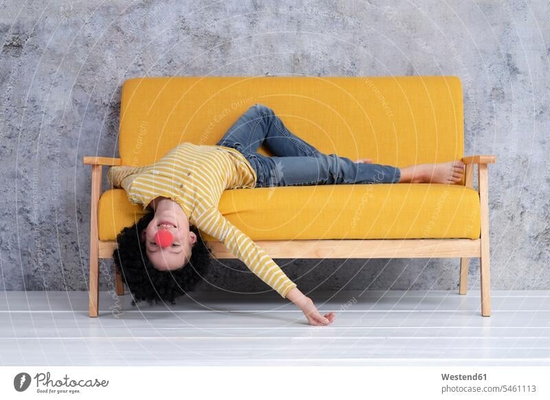 Boy with red clown nose and black hair on yellow couch clowns jumper sweater Sweaters couches settee settees sofa sofas smile relax relaxing relaxation delight