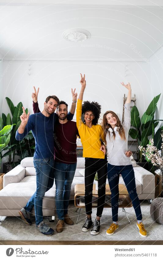 Portrait of four happy friends standing side by side in living room mate jumper sweater Sweaters couches settee settees sofa sofas headphone headset smile