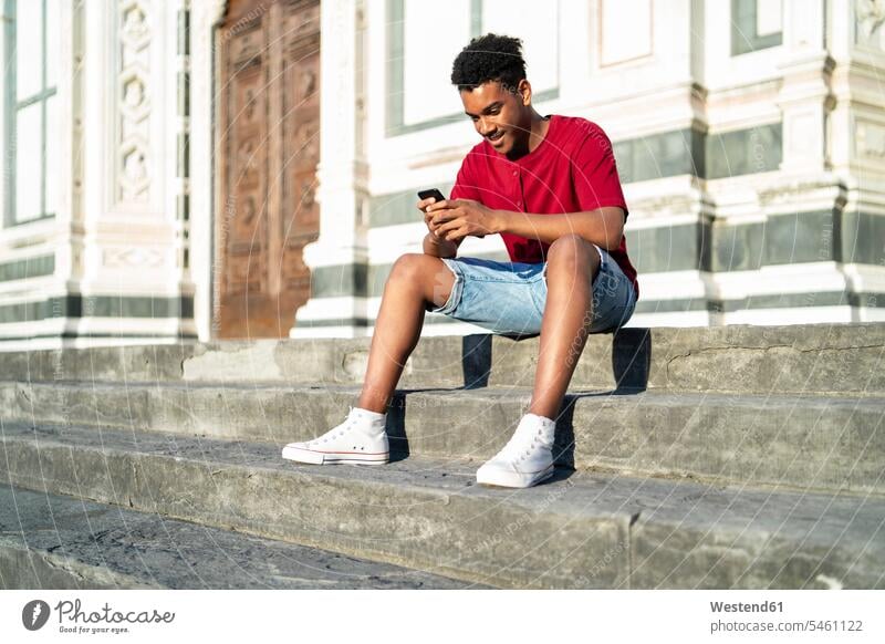 Young man sitting on outdoor stairs checking his smartphone, Florence, Italy human human being human beings humans person persons African black black ethnicity