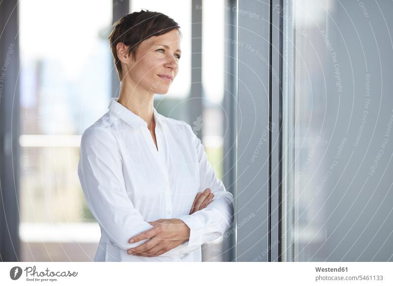 Businesswoman in office looking out of window smiling smile businesswoman businesswomen business woman business women offices office room office rooms windows