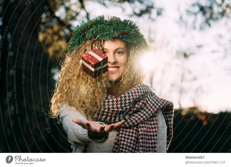 Portrait of smiling young woman with Christmas wreath on her head juggling with Christmas present scarfs scarves juggle in the evening delight enjoyment