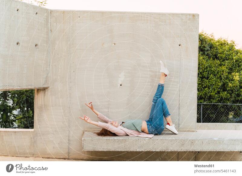 Young redheaded woman with raised arms lying on concrete bench benches in the evening Ardor Ardour enthusiasm enthusiastic excited enjoy enjoyment indulgence