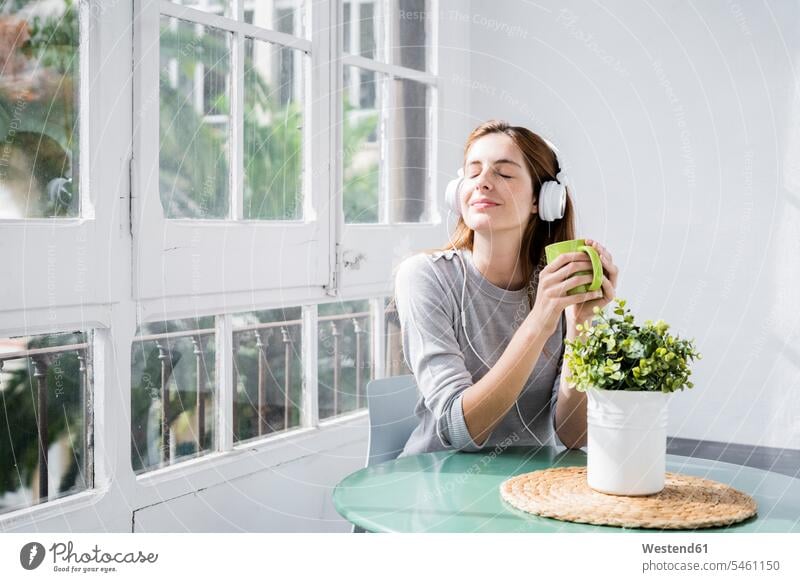 Young woman stting at the window at home with coffee cup and headphones human human being human beings humans person persons celibate celibates singles
