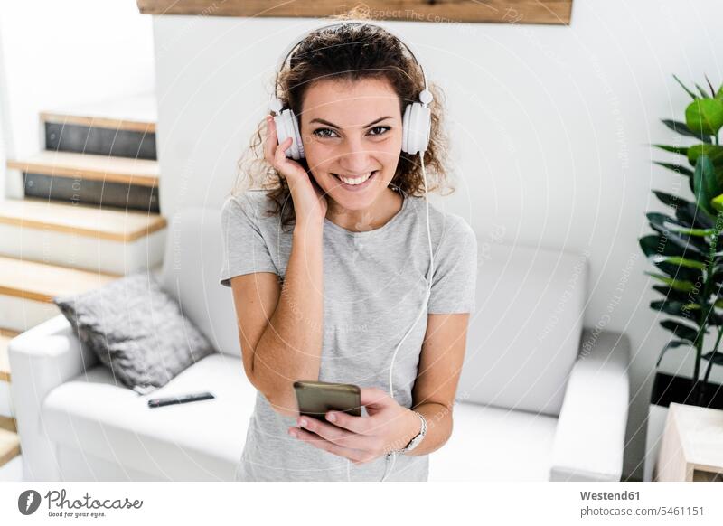 Portrait of smiling young woman listening music with headphones and cell phone T- Shirt t-shirts tee-shirt couches settee settees sofa sofas headset