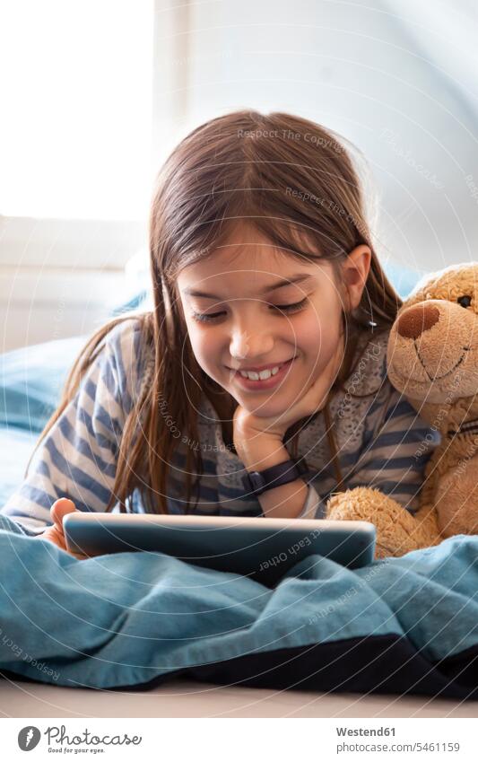 Portrait of smiling girl lying on bed with teddy bear using digital tablet Bed - Furniture beds teddies teddy bears teddy-bear relax relaxing smile play