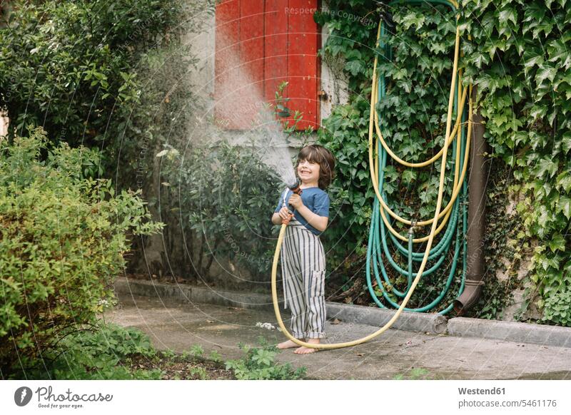 Boy enjoying holding garden hose while watering plants at backyard rural scene Non Urban Scene Non-Urban Scene non-urban color image colour image outdoors