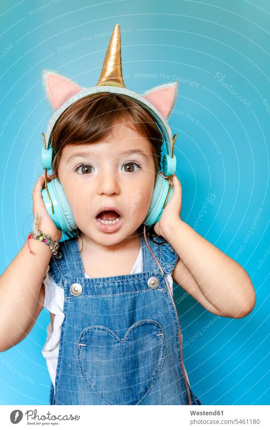 Portrait of cute little girl listening music and singing with unicorn shaped earphones on blue background human human being human beings humans person persons