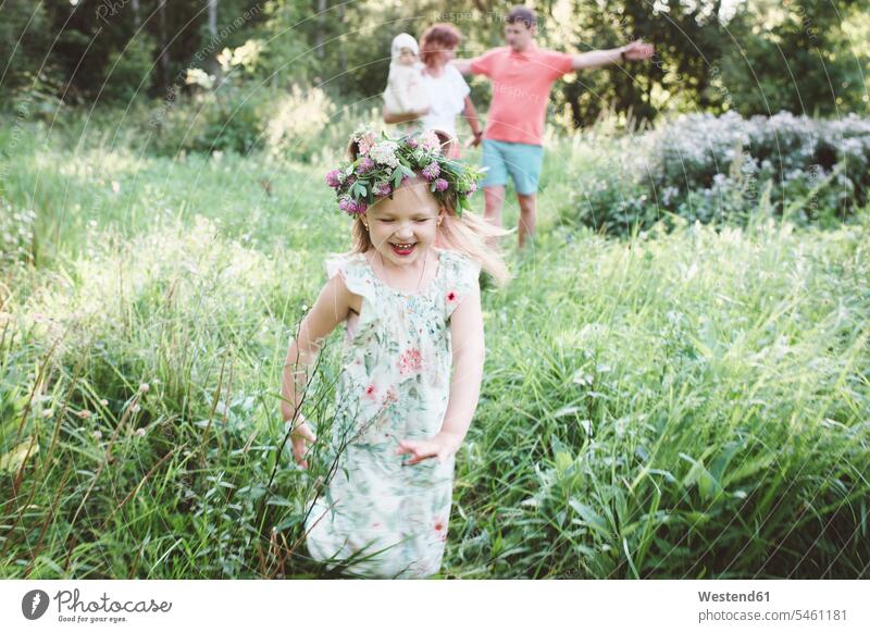 Happy little girl with flower wreath running from her parents in nature human human being human beings humans person persons caucasian appearance