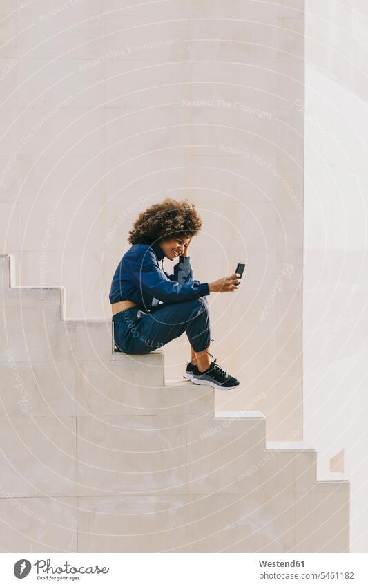 Stylish young woman wearing tracksuit and using cell phone on outdoor stairs human human being human beings humans person persons curl curled curls curly hair
