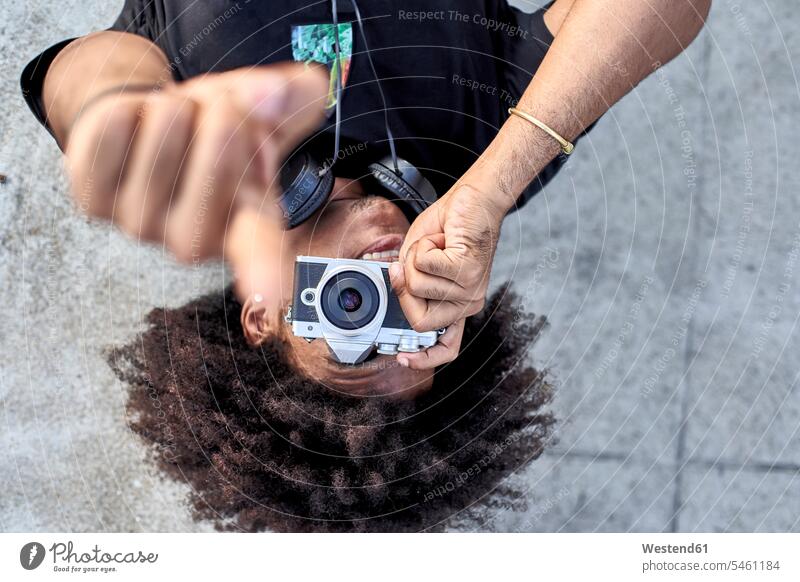 Young man laying on wall and taking pictures with his camera and pointing with his finger photographers images photographs photos headphone headset cameras