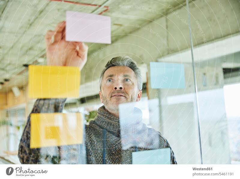 Male mature businessman putting note on glass wall while working at office color image colour image indoors indoor shot indoor shots interior interior view