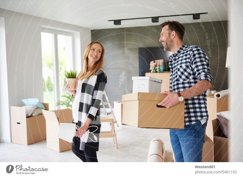Happy couple moving house carrying cardboard box and plant cardboard boxes packing case packing cases twosomes partnership couples Plant Plants flat flats