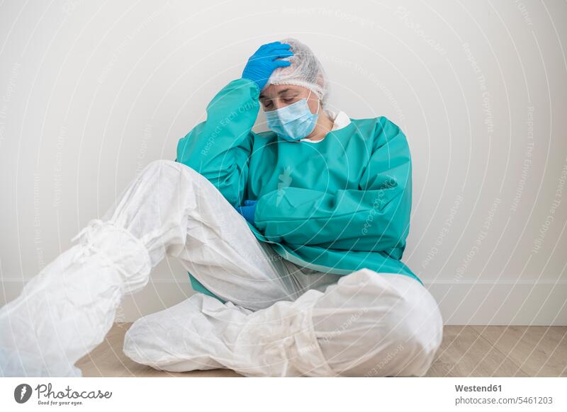 Exhausted woman wearing personal protective equipment sitting on the floor Occupation Work job jobs profession professional occupation health healthcare