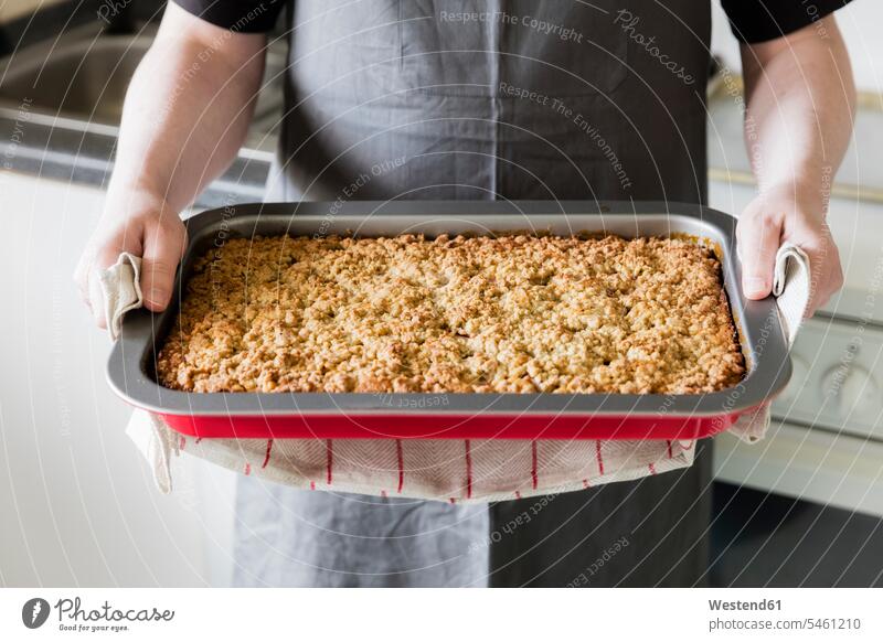 Man in kitchen holding baking tray with homemade rhubarb cake, partial view man men males home made home-made baking trays domestic kitchen kitchens Adults