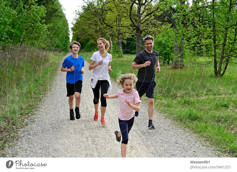 Children running with parents on dirt road amidst trees and plants in forest color image colour image Germany wood woods forests nature natural world