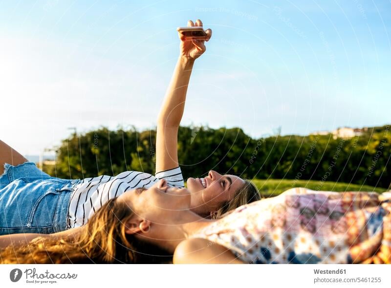 Smiling young woman taking selfie with female friend while relaxing on field during sunny day color image colour image outdoors location shots outdoor shot