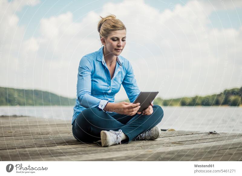 Woman sitting on jetty at a lake using tablet jetties lakes digitizer Tablet Computer Tablet PC Tablet Computers iPad Digital Tablet digital tablets woman