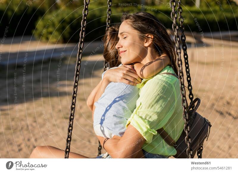 Smiling mother hugging daughter on a playground embracing embrace Embracement play yard play ground playgrounds daughters smiling smile mommy mothers ma mummy