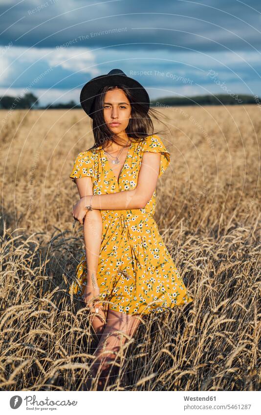 Portrait of young woman wearing summer dress with floral design and a hat dancing in corn field Grain field Cornfield Corn Field Cornfields Corn Fields
