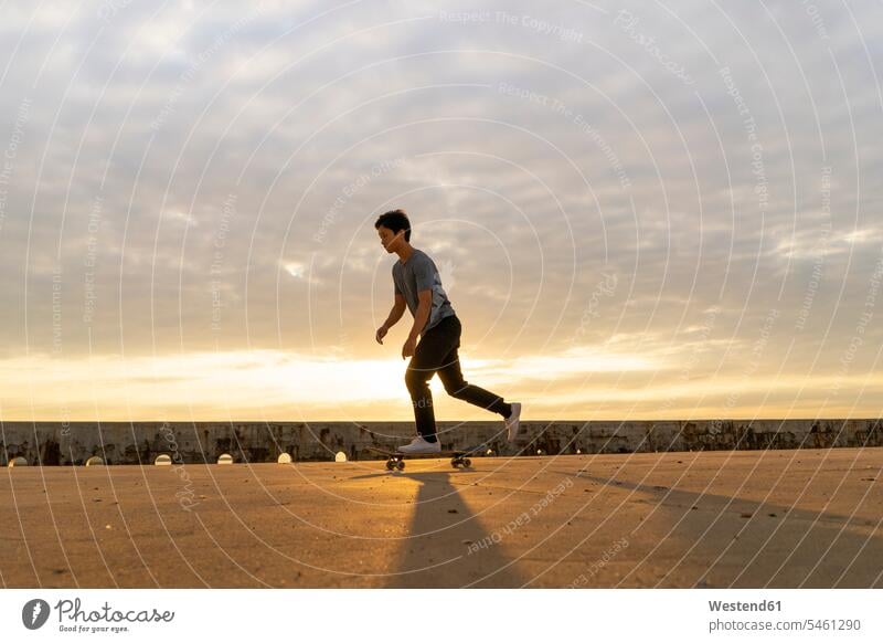 Young Chinese man skateboarding at sunsrise near the beach Chinese Ethnicity young Skate Board skateboards beaches skateboarder skater skateboarders skaters