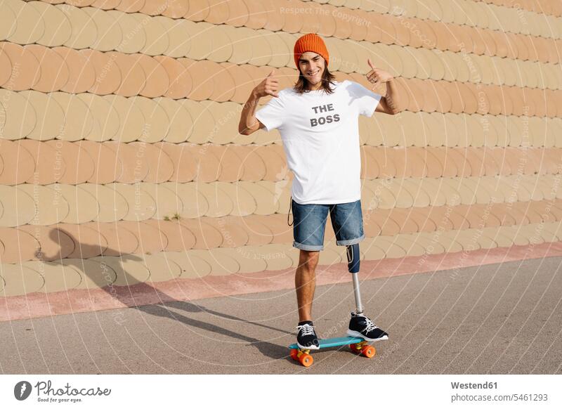 Young disabled man standing on skateboard at sports court color image colour image outdoors location shots outdoor shot outdoor shots day daylight shot