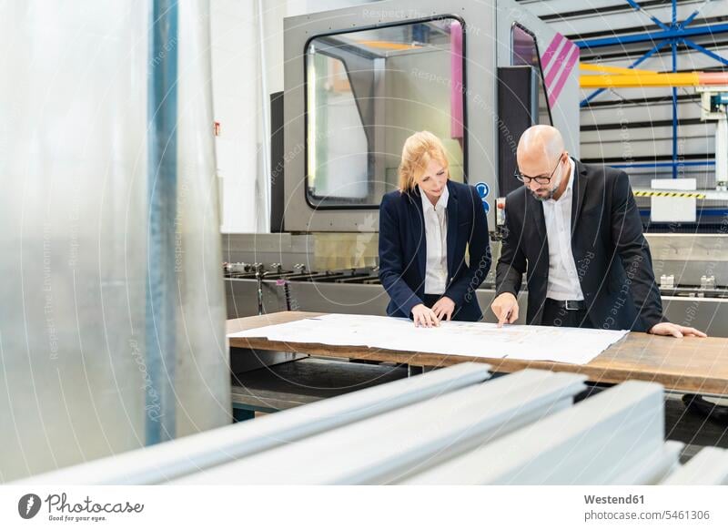 Businessman and businesswoman looking at plan on table in factory eyeing Table Tables factories Business man Businessmen Business men businesswomen