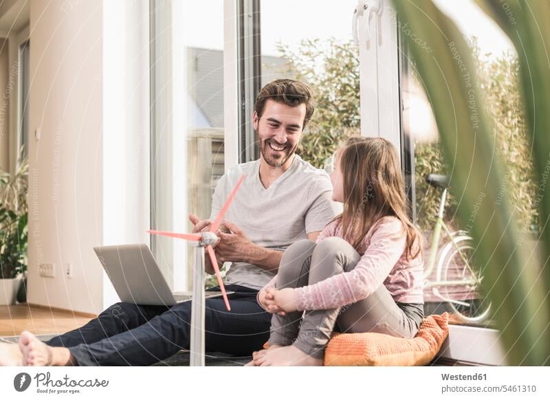 Young man and little girl playing with model of a wind turbine Germany sitting on ground Sitting On The Floor Sitting On Floor using laptop using a laptop