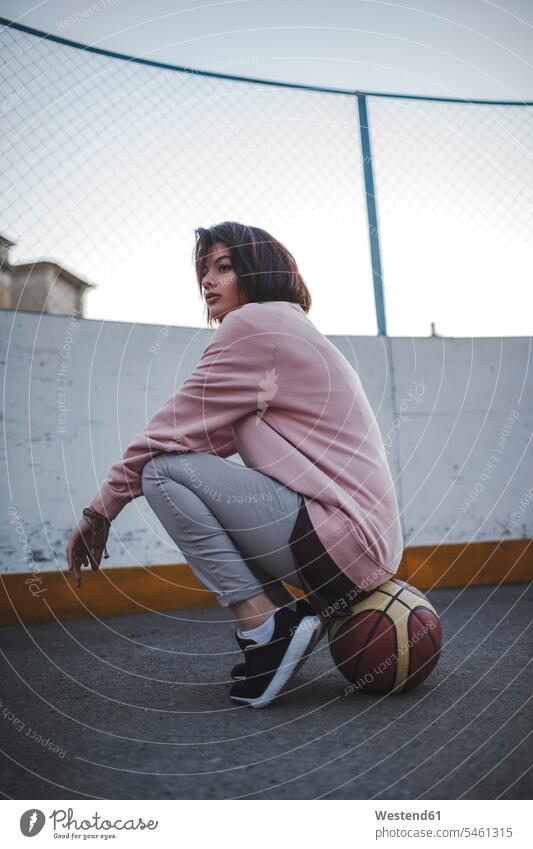 Young woman sitting on basketball outdoors females women fence fences basketballs Adults grown-ups grownups adult people persons human being humans human beings