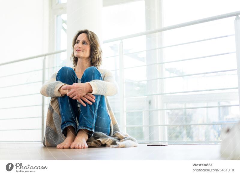Relaxed woman sitting on the floor at home relaxed relaxation floors Seated smiling smile females women relaxing Adults grown-ups grownups adult people persons