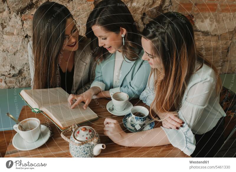 Three young women reading a book in a cafe Spain fashionable rustic brickwork stonework togetherness sharing share Tea Cup Tea Cups Teacup Teacups Intelligence