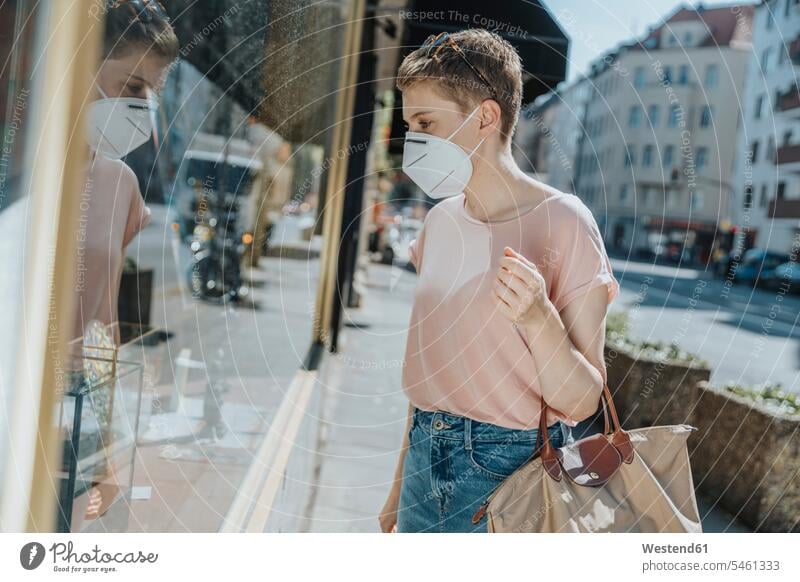 Woman wearing protective face mask doing window shopping while standing on street in city color image colour image outdoors location shots outdoor shot
