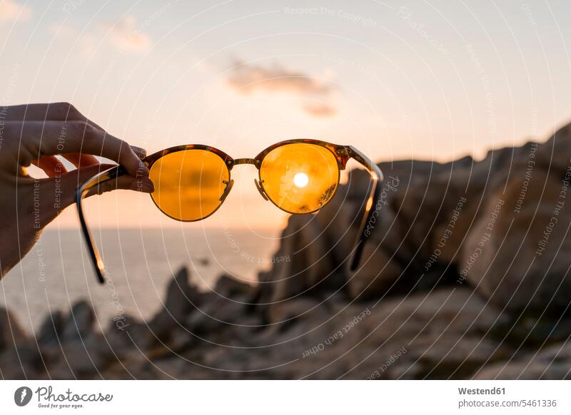 Man's hand holding sunglasses in front of evening sun, close-up sun glasses Pair Of Sunglasses human hand hands human hands men males people persons human being