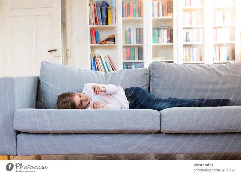 Girl lying on couch at home holding cell phone mobile phone mobiles mobile phones Cellphone cell phones laying down lie lying down settee sofa sofas couches