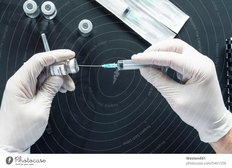 Cropped image of doctor's hand injecting syringe in vaccination vial over laptop at laboratory desk color image colour image indoors indoor shot indoor shots